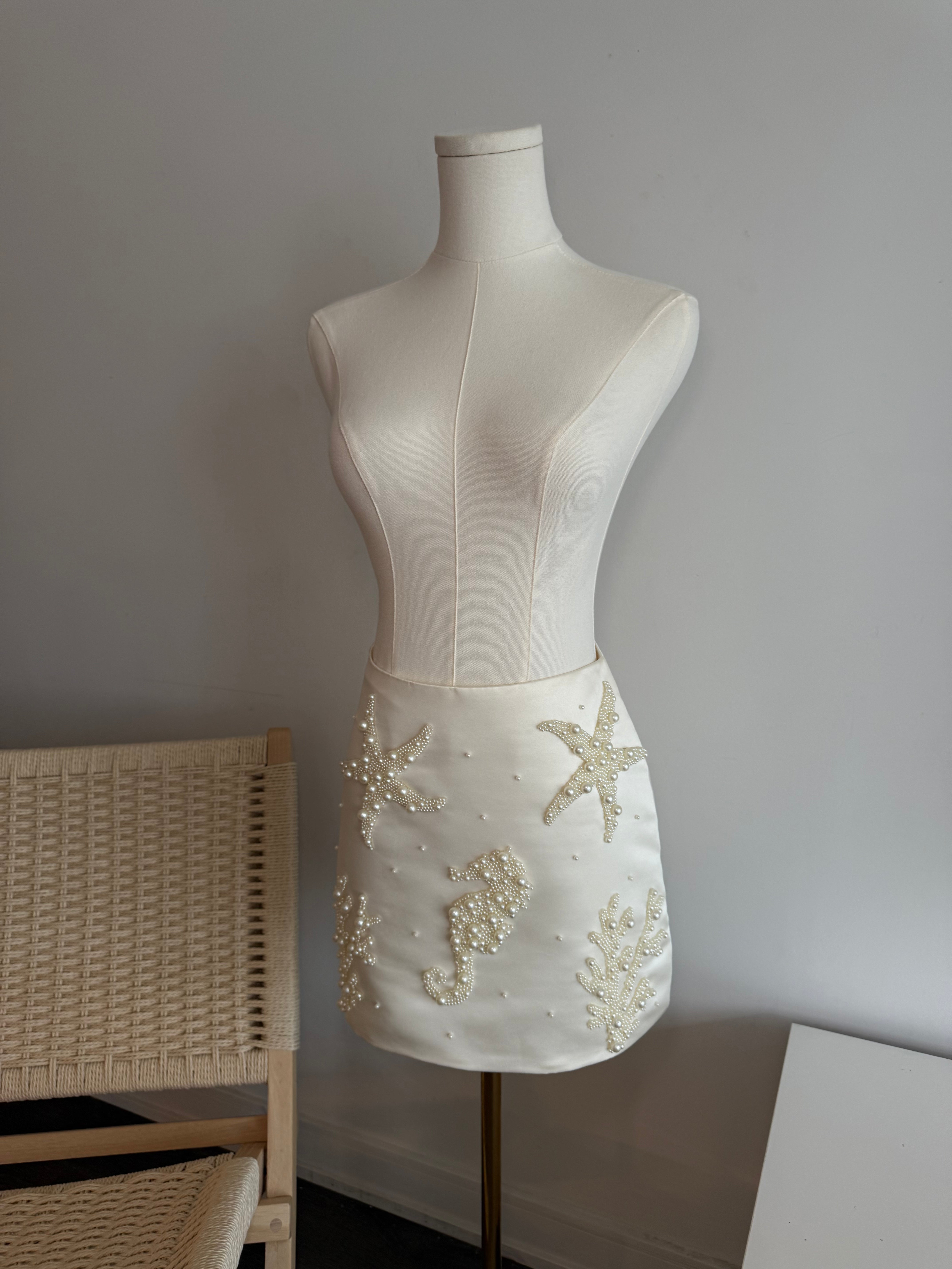 Hoekey ivory satin mini skirt adorned with pearl starfish, seahorse, and coral appliqué, designed with intricate beading for a luxe ocean-inspired look.
