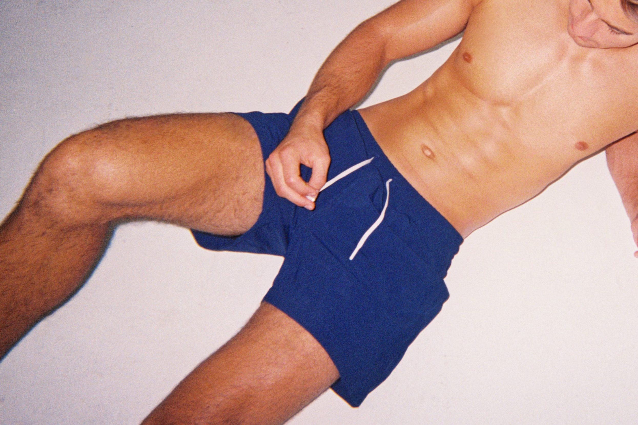 Man wearing blue Hoekey swim shorts reclining on a light background, showcasing fit and style of men’s swimwear.