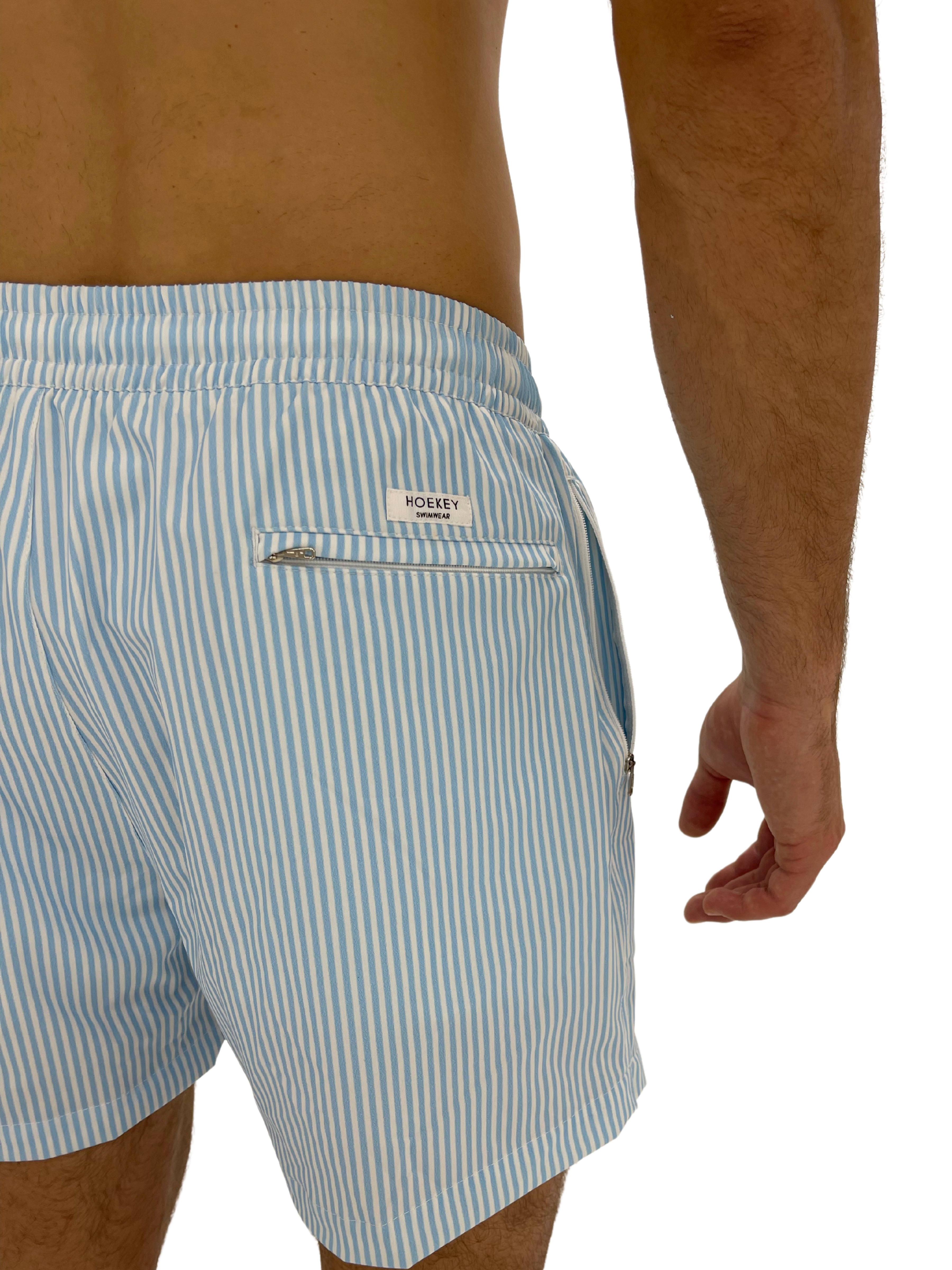 Hoekey blue and white striped men’s swim shorts featuring quick-dry fabric, elastic waistband, and secure back zippered pocket with logo detail.