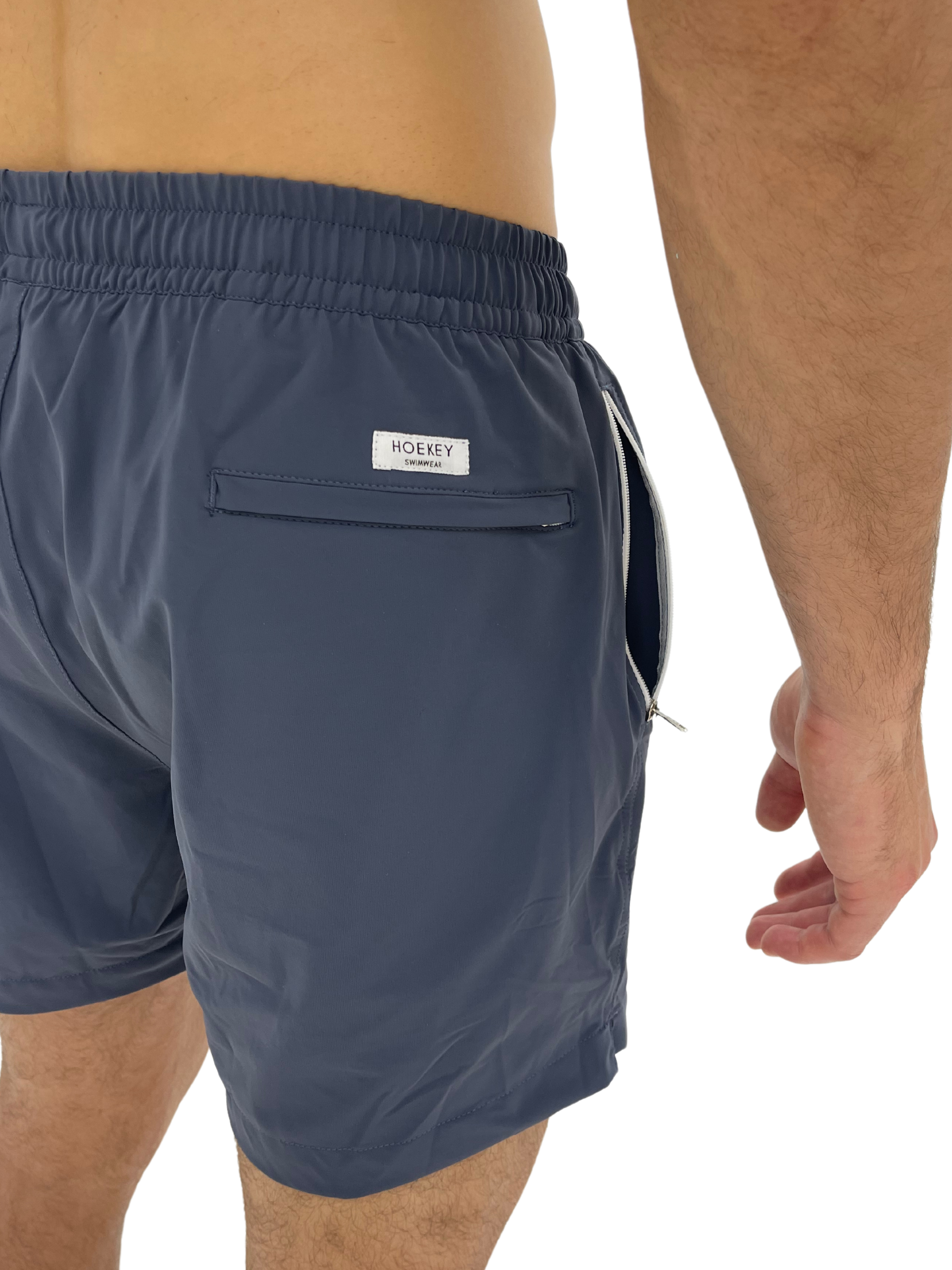 Hoekey gray men’s swim shorts showcasing back pocket with branded logo patch, quick-dry fabric, and secure side zippered pocket for practicality and modern style.