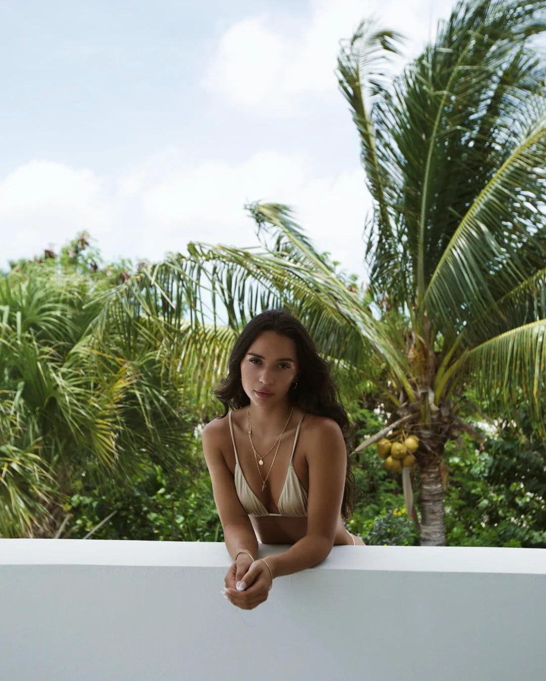 beige triangle bikini on model leaning on balcony with palm trees in the background