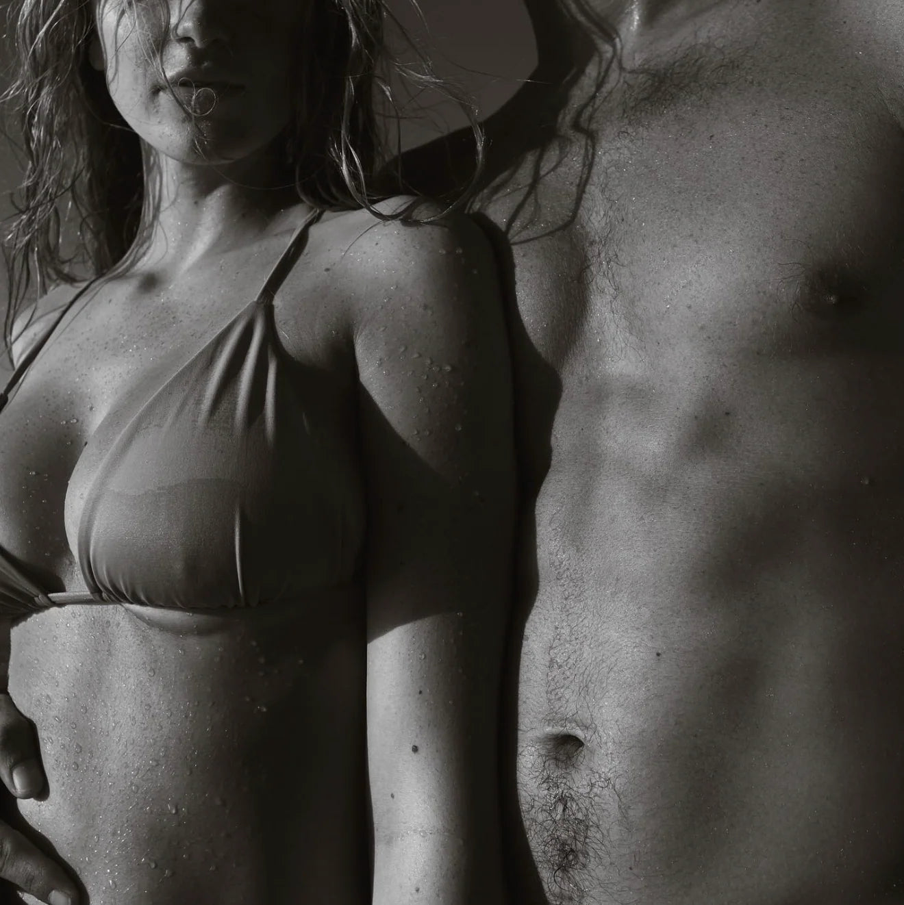black and white close up of wet triangle bikini top beside male torso after swim